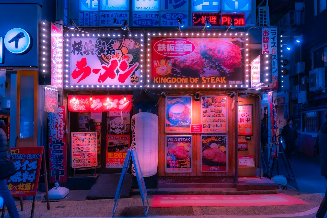 A neon-lit storefront glowing red and pink on a Japanese street at night