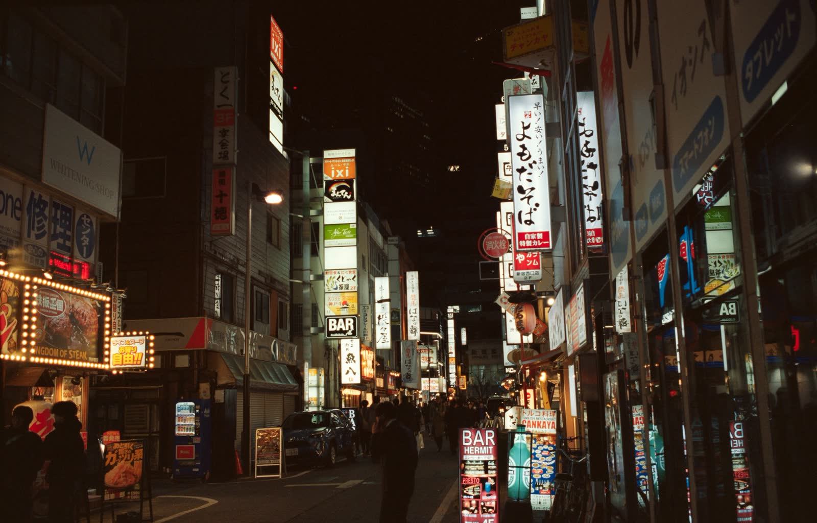 A dark city street lit by scattered neon signage